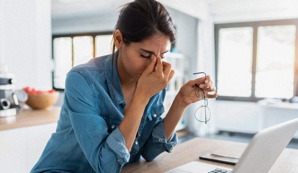 femme avec un ordinateur tenant des lunettes et ayant l'air fatiguée, ce qui peut être un symptôme de problèmes de thyroïde
