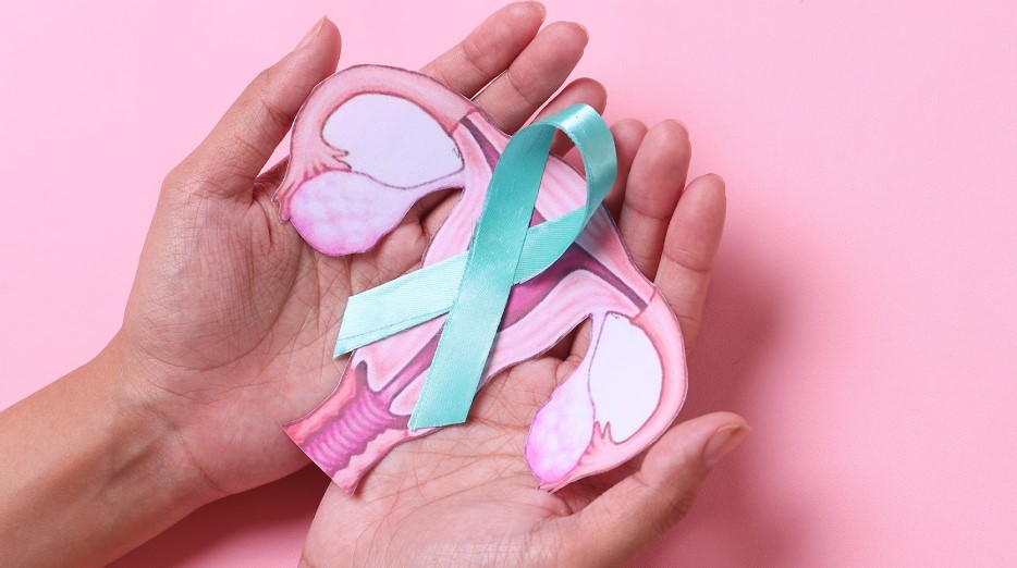 Teal ovarian cancer awareness ribbon with uterus shape on a doctor's palm over a pink background.