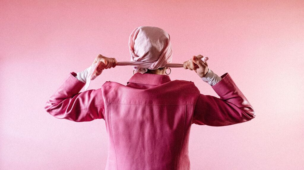 Femme vue de dos, vêtue entièrement de noir, portant un foulard rose sur la tête symbolisant la force face au cancer du sein.