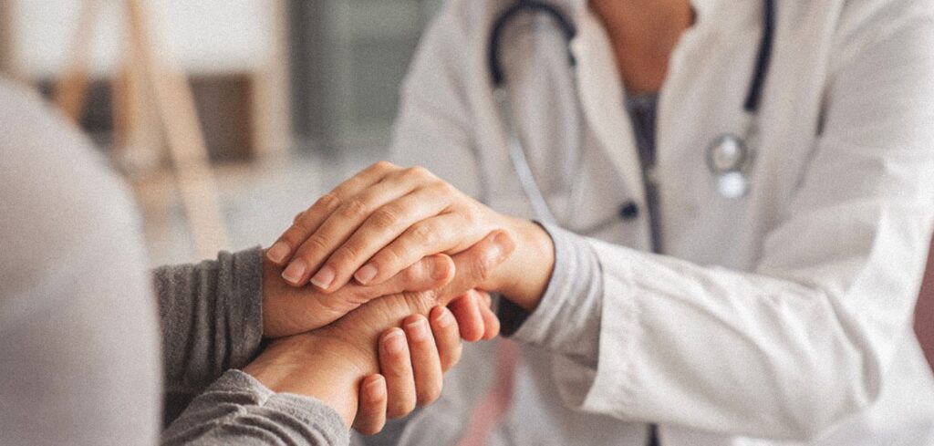 Une travailleuse de la santé tenant les mains d'une patiente pour la réconforter lors d'un diagnostic difficile.

