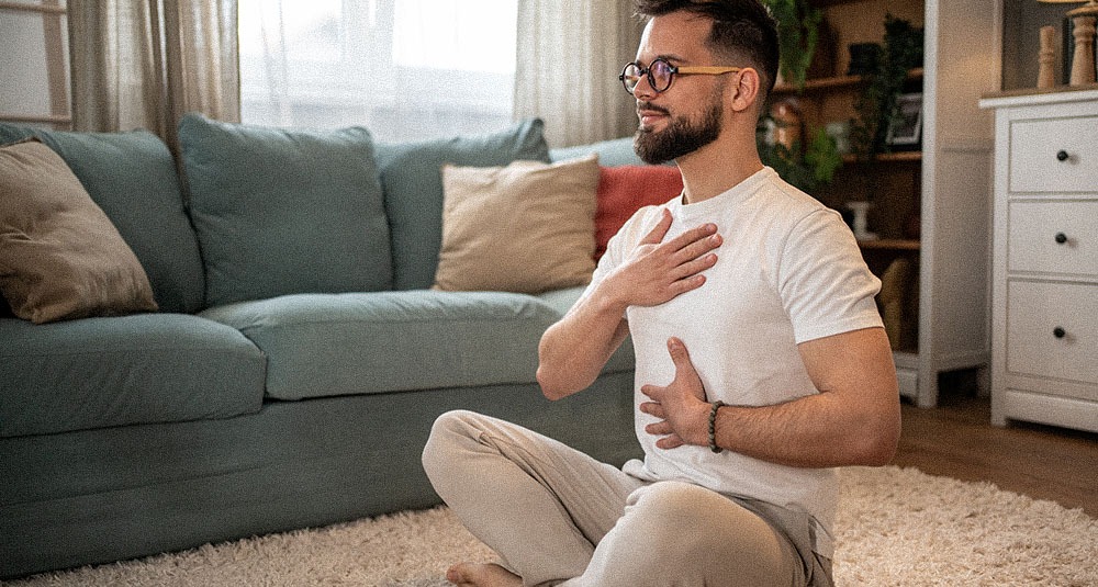 A man managing stress by deep breathing and meditating in his living room.