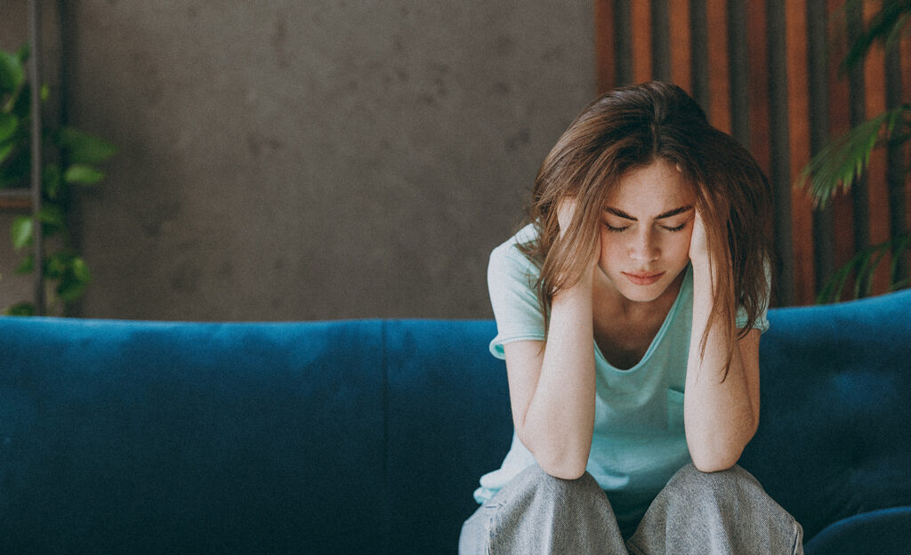 Exhausted woman in her thirties wearing casual clothes, holding her head in her hand with her eyes closed to signify tiredness.