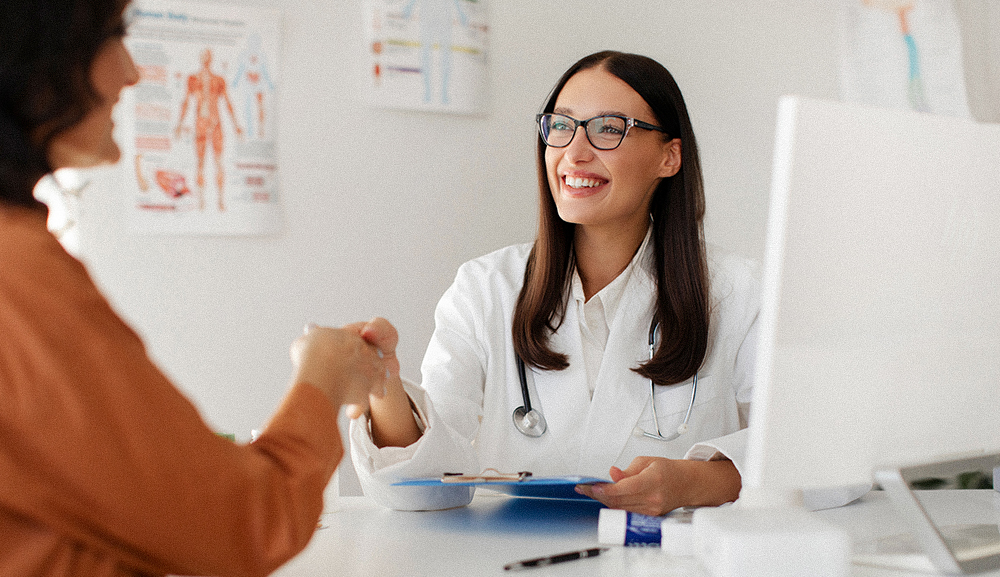Cheerful female doctor and female patient handshaking during a check-up at the doctor's office.