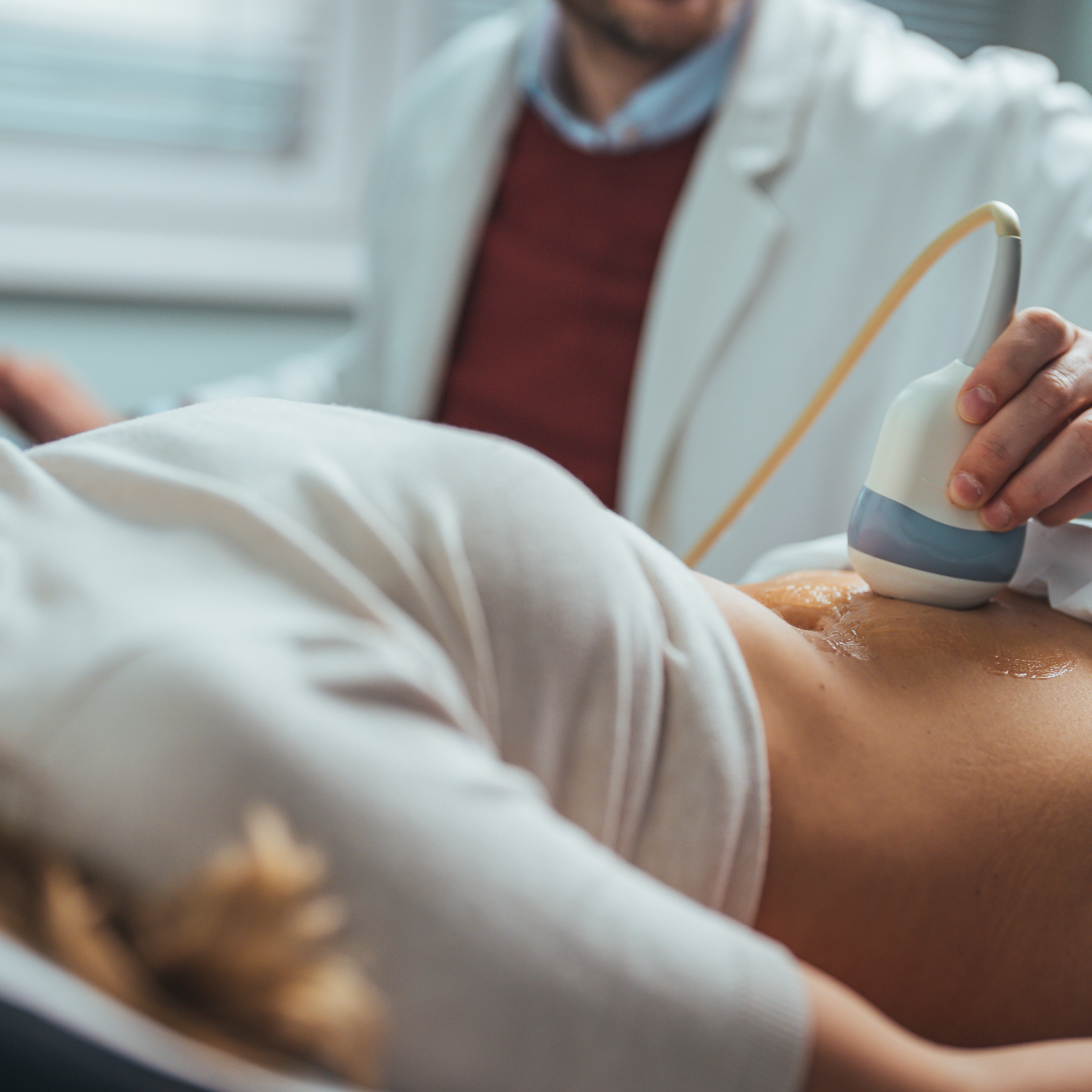 Doctor makes the patient women abdominal ultrasound. Ultrasound Scanner in the hands of a doctor. Diagnostics. Sonography. Close-up Of Doctor Moving Ultrasound Probe On Pregnant Woman's Stomach In Hospital