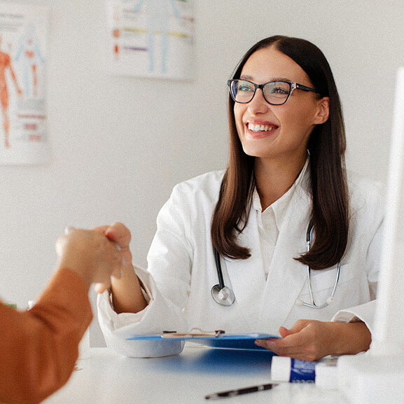 Medical services concept. Cheerful woman doctor and female patient handshaking during meeting in clinic, therapist welcoming lady