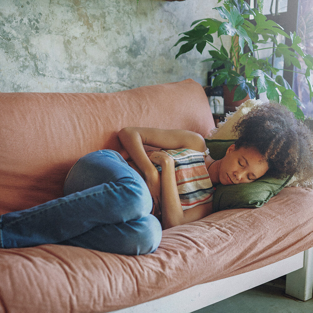 Shot of a young woman experiencing stomach pain while lying on the sofa at home stock photo