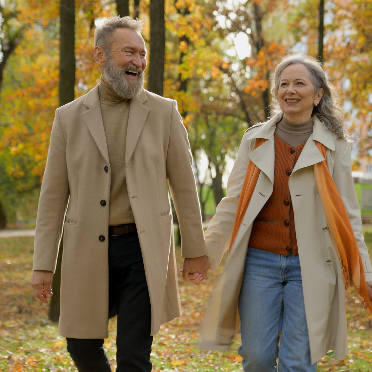 Happy old senior married couple adults hold hands together walking in city park joyful mature gray haired Caucasian woman wife and man husband have fun talking laughing walk stroll in autumn forest. High quality 4k footage
