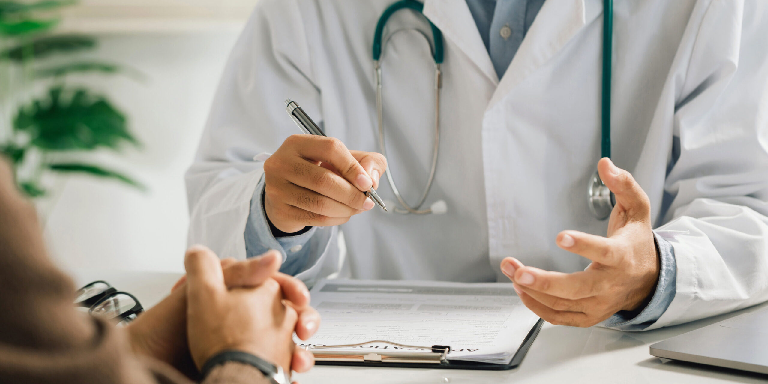A professional physician in a white medical uniform talks to discuss results or symptoms and gives a recommendation to a male patient and signs a medical paper at an appointment visit in the clinic.