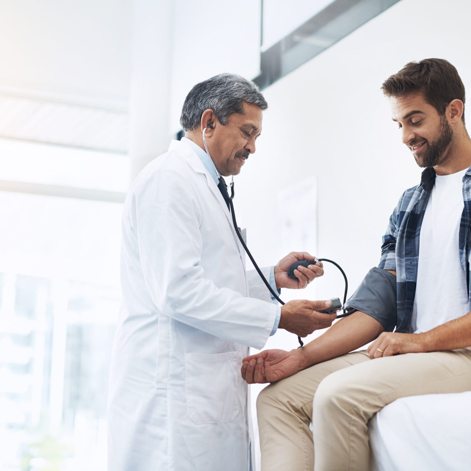 Healthcare, patient and doctor with blood pressure test, help and wellness checkup of person at hospital. Medicine, health care expert and Indian man in doctors office consulting medical professional.